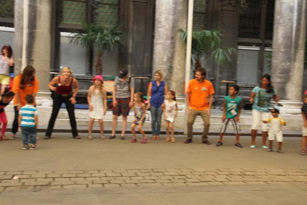 Eine Gruppe von Erwachsenen und Kindern steht auf einer Straße vor einem Gebäude.