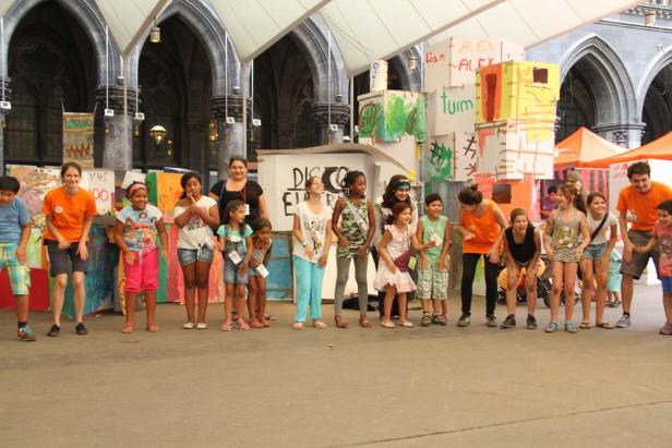 Eine Gruppe Kinder und Erwachsene steht vor einer Bühne mit bemalten Kulissen.