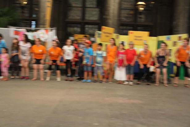 Eine Gruppe von Kindern und Erwachsenen steht in einer Reihe vor gelben Schildern.