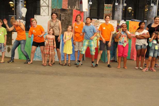 Eine Gruppe von Kindern und Erwachsenen steht vor einer bemalten Kulisse.