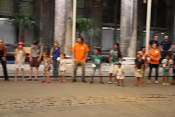 Eine Gruppe von Kindern und Erwachsenen steht vor einem Gebäude mit Säulen.