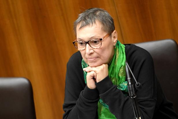 Eine Frau mit Brille und grünem Schal sitzt nachdenklich da.