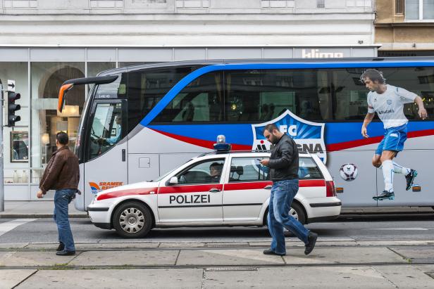 Ein Mann überquert die Straße vor einem Bus mit Fußballwerbung und einem Polizeiauto.