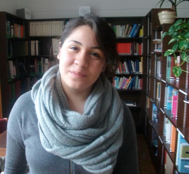 Eine Frau mit grauem Schal steht vor einem Bücherregal.