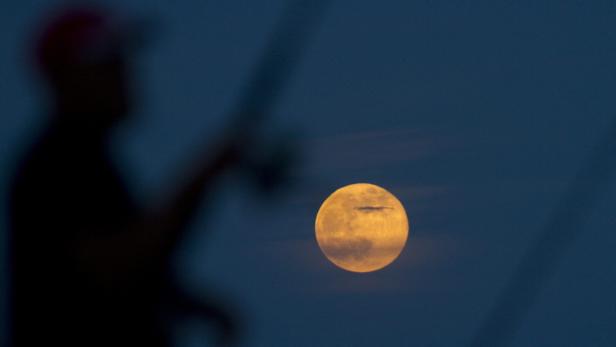 Ein unscharfer Mann betrachtet den hellen Vollmond am dunklen Himmel.
