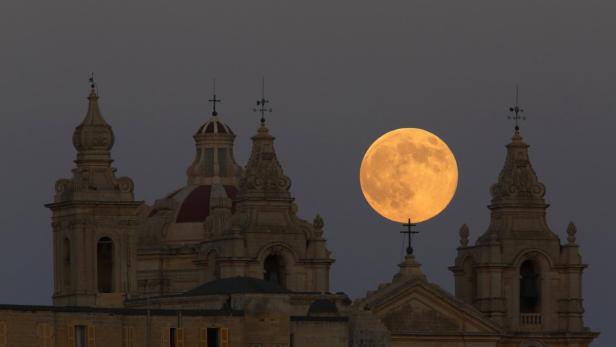 Der Vollmond geht über den Türmen einer Kirche auf.