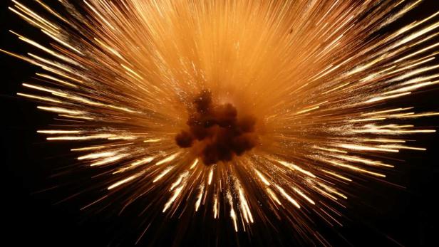 Eine Explosion erhellt den dunklen Nachthimmel mit goldenen Funken.