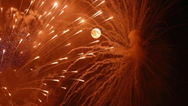 Feuerwerk erhellt den Nachthimmel mit dem Mond im Hintergrund.
