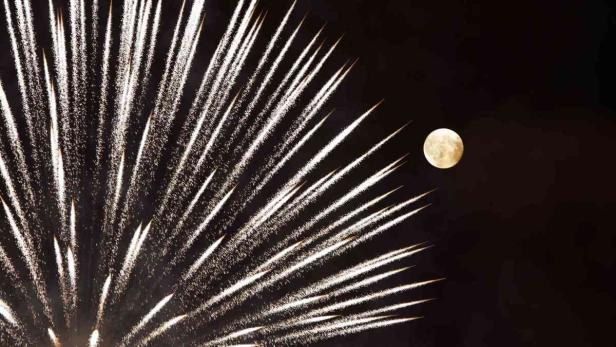 Feuerwerk erhellt den Nachthimmel neben dem Vollmond.