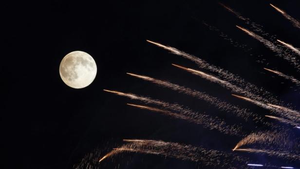 Der Vollmond leuchtet neben aufsteigendem Feuerwerk am Nachthimmel.