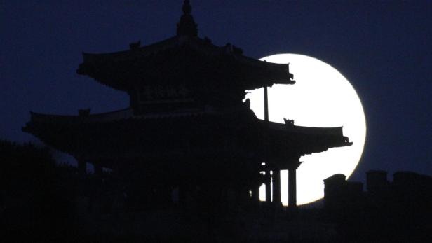Die Silhouette eines chinesischen Tempels vor einem hellen Vollmond.