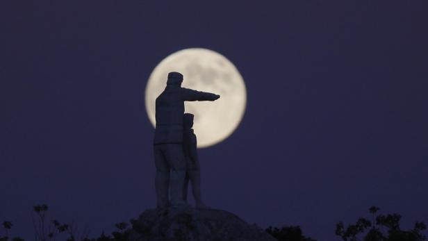 Eine Statue von zwei Personen vor einem Vollmond am Nachthimmel.