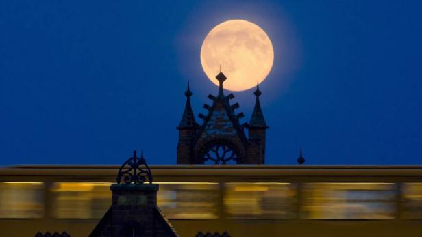 Ein Zug fährt vor einem Gebäude mit einem großen Vollmond im Hintergrund.