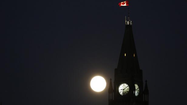 Der Vollmond scheint neben dem Peace Tower in Ottawa, auf dem eine kanadische Flagge weht.