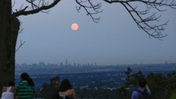 Menschen beobachten den aufgehenden Vollmond über der Skyline von New York City.