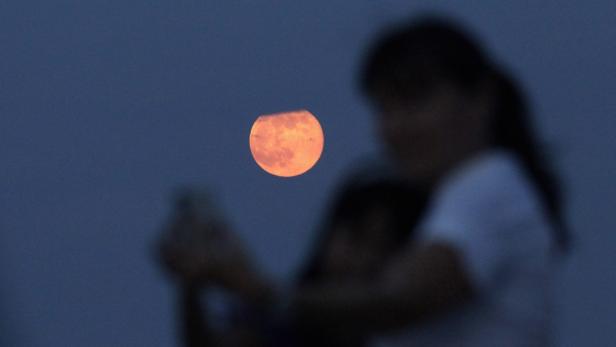 Eine verschwommene Person fotografiert den orangefarbenen Mond am Himmel.