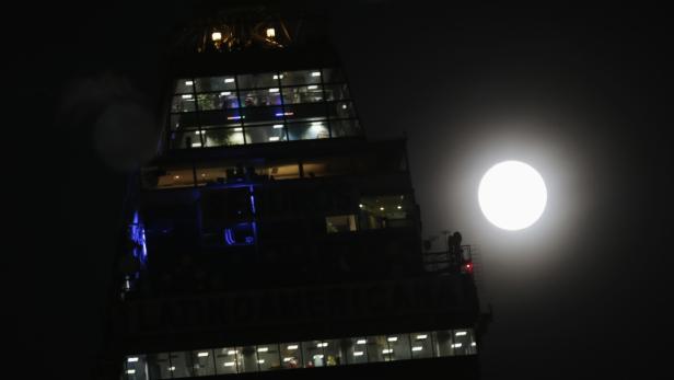 Ein Gebäude mit beleuchteten Fenstern vor einem hellen Vollmond.