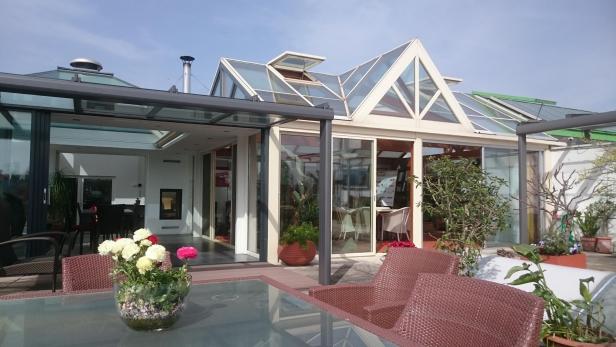 Ein Wintergarten mit Glasdach und Gartenmöbeln auf einer Terrasse.