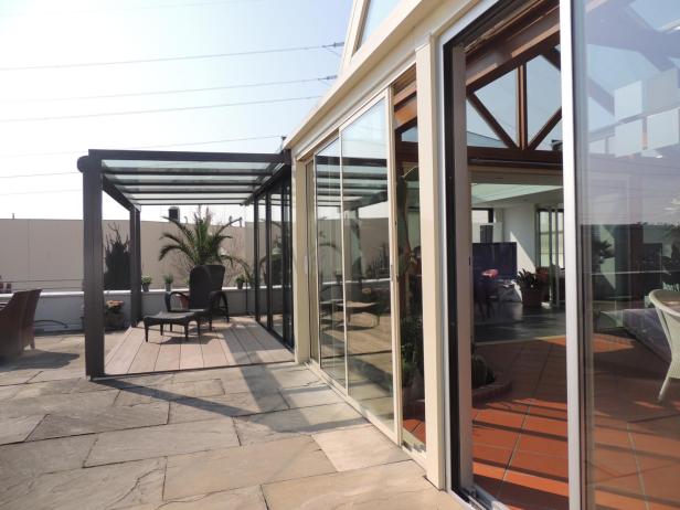 Ein Wintergarten mit Schiebetüren führt auf eine Terrasse mit Pergola.