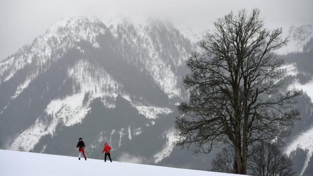 Zwei Personen beim Skilanglauf vor einer verschneiten Berglandschaft.