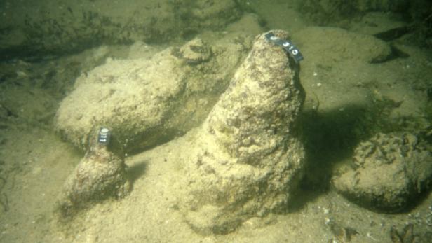 Unterwasseraufnahme von Amphoren, die auf dem sandigen Meeresboden liegen.
