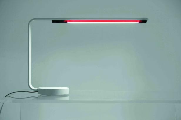 Eine moderne Schreibtischlampe mit rotem und weißem Licht steht auf einem Tisch.