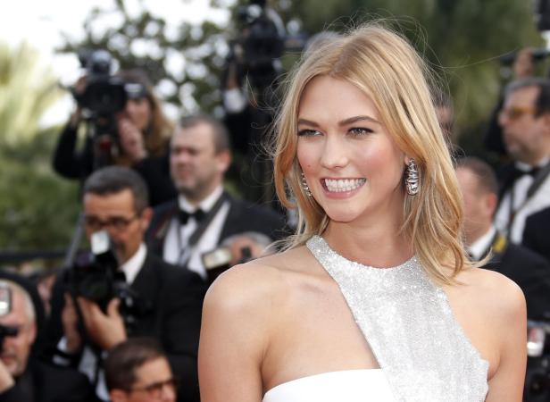 Karlie Kloss lächelt auf dem roten Teppich in einem weißen Kleid mit silbernen Details.