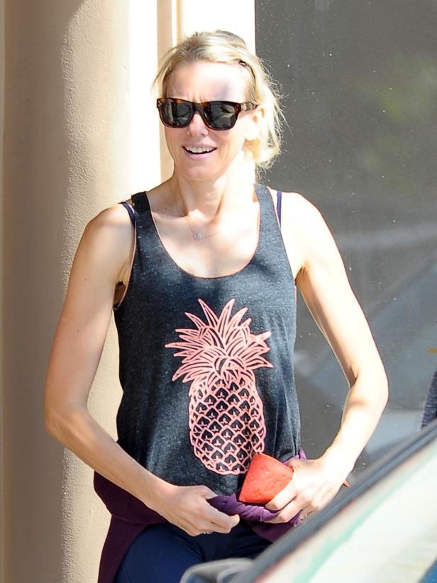Naomi Watts mit Sonnenbrille und Ananas-Tanktop hält einen roten Gegenstand in der Hand.
