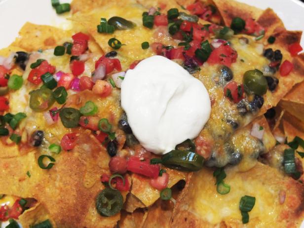 Ein Teller Nachos mit Käse, Jalapeños, Tomaten, schwarzen Bohnen und einem Klecks saurer Sahne.