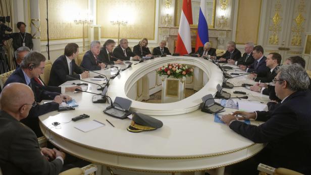 Offizielle Zusammenkunft von Diplomaten an einem ovalen Tisch mit den Flaggen Österreichs und Russlands.