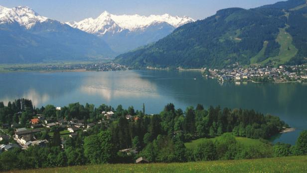 Blick auf einen See mit Bergen im Hintergrund und einer Stadt am Ufer.