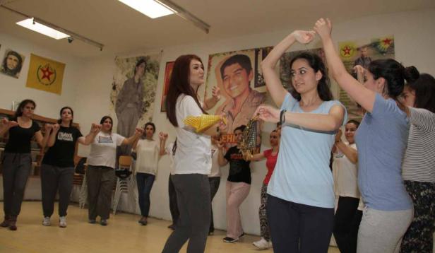 Eine Gruppe Frauen tanzt in einem Raum mit politischen Postern an den Wänden.