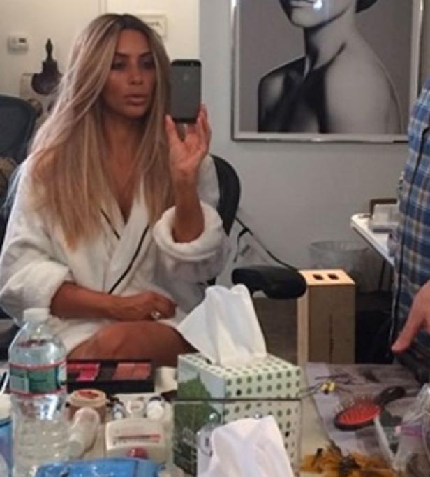 Kim Kardashian macht ein Selfie in einem weißen Bademantel vor einem Schminktisch.