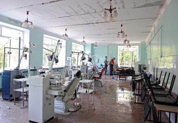 Ein zerstörtes Zahnarztzimmer mit umgestürzten Stühlen und Trümmern auf dem Boden.