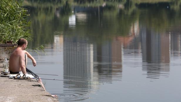 Ein Mann sitzt am Ufer eines Sees und angelt.