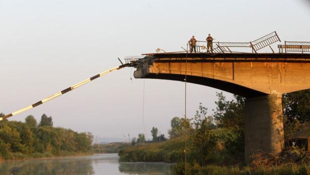 Zwei Soldaten stehen auf einer zerstörten Brücke über einem Fluss.