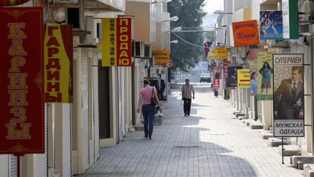 Eine Gasse mit Geschäften, an denen Werbeschilder hängen, und Passanten.