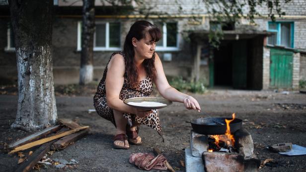 Eine Frau kocht im Freien auf einem improvisierten Feuer.