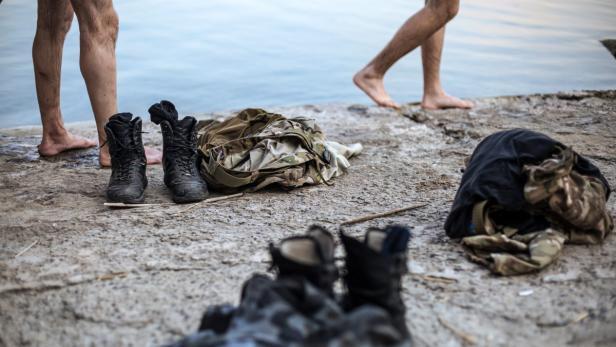 Am Ufer stehen Stiefel und Kleidung, während Personen ins Wasser gehen.