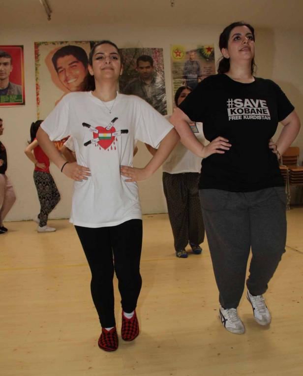 Zwei Frauen tanzen in T-Shirts mit politischen Botschaften in einem Raum.