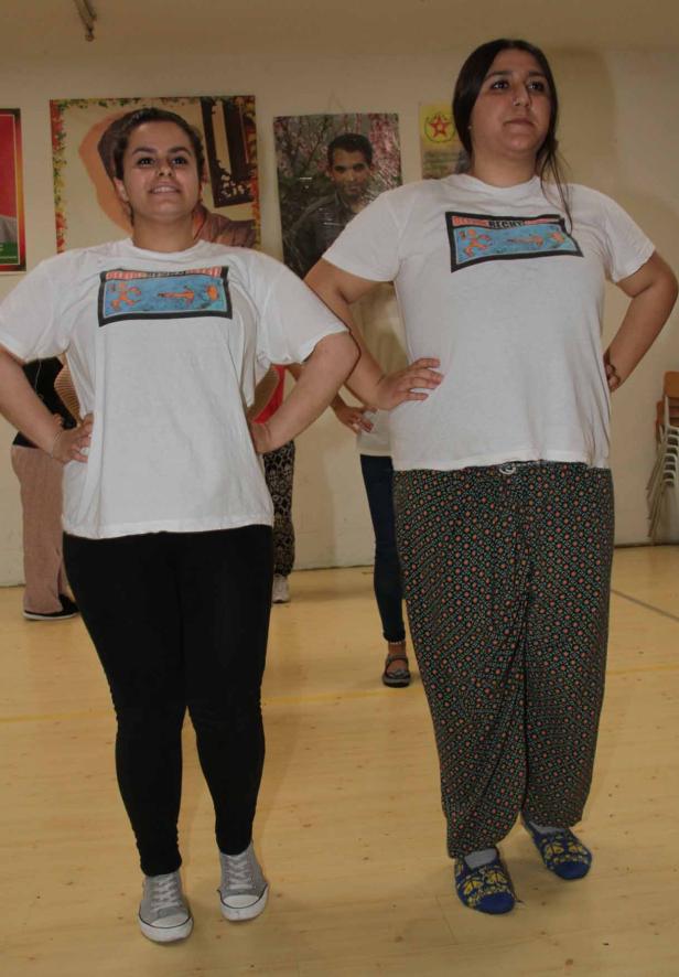 Zwei Frauen stehen mit T-Shirts und gemusterten Hosen in einem Raum.