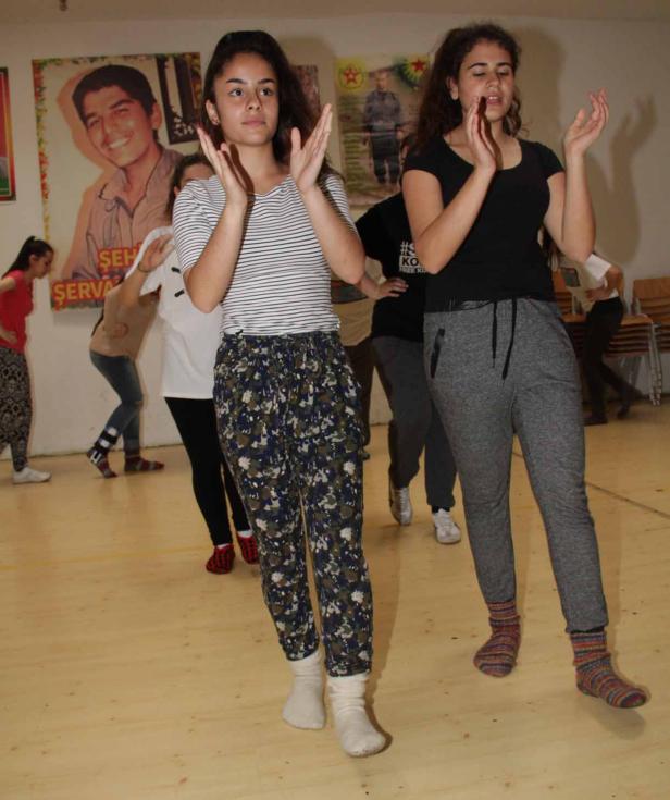 Eine Gruppe junger Leute tanzt in einem Raum mit Postern an der Wand.