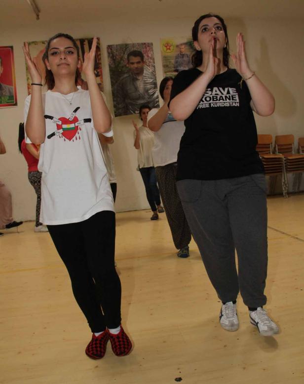Eine Gruppe von Frauen tanzt in einem Raum mit kurdischen Symbolen an den Wänden.