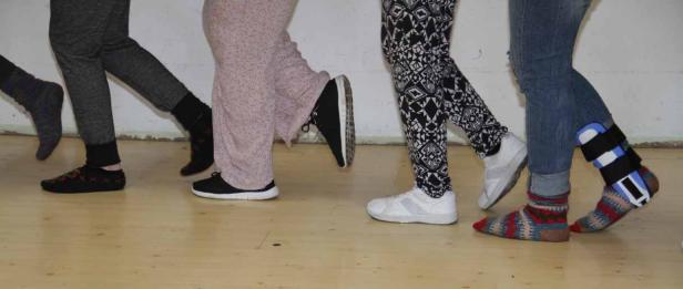 Eine Reihe von Personen, von denen nur die Beine zu sehen sind, stehen auf einem Holzboden.