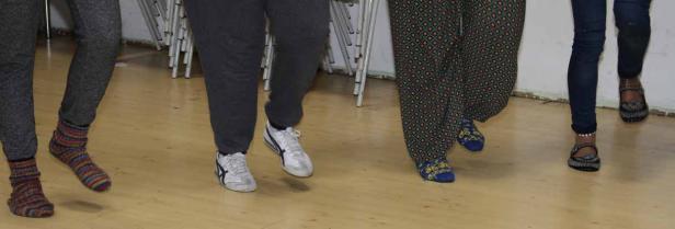 Mehrere Personen sind barfuß oder mit Socken und Schuhen auf einem Holzboden zu sehen.