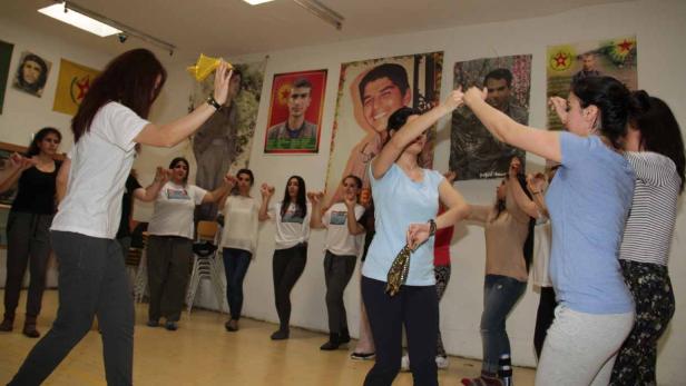 Eine Gruppe von Frauen tanzt in einem Raum mit politischen Postern an der Wand.