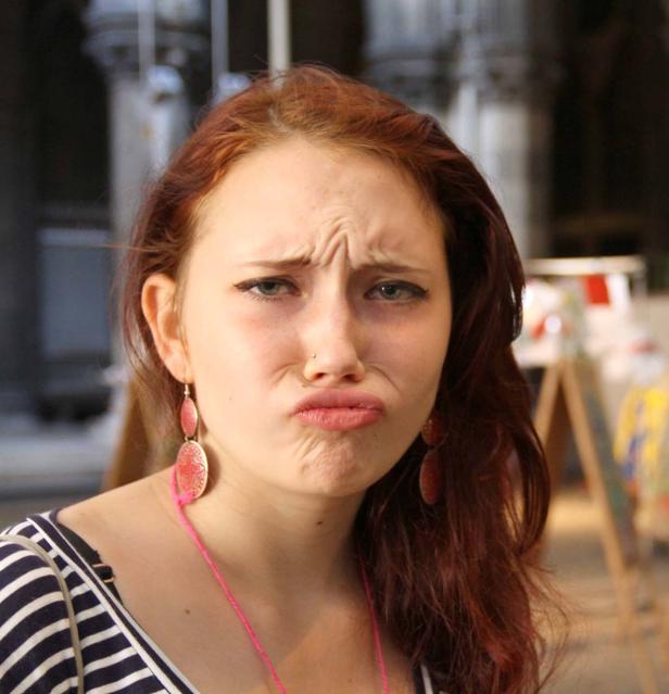 Eine junge Frau mit roten Haaren zieht eine Schmollmund und runzelt die Stirn.