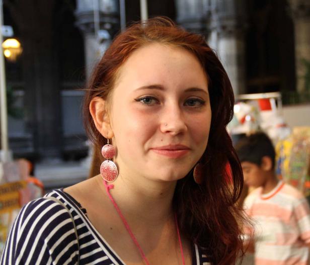 Eine junge Frau mit roten Haaren und Ohrringen lächelt.