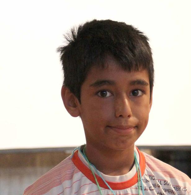 Ein junger Mann mit dunklen Haaren und einem gestreiften T-Shirt lächelt leicht.