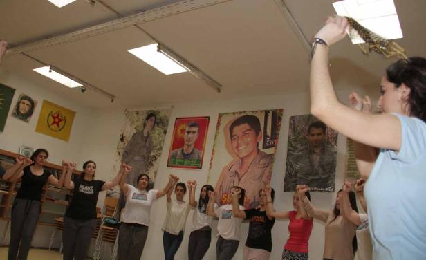 Eine Gruppe von Frauen steht in einem Raum mit politischen Postern und erhobenen Fäusten.